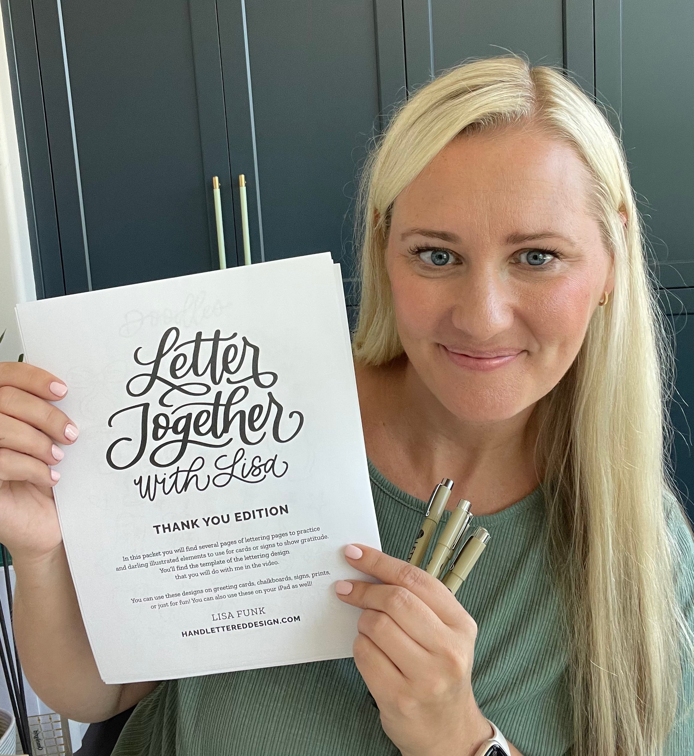 Woman holding a 'Letter Together with Lisa' book and pen set in front of a dark cabinet.